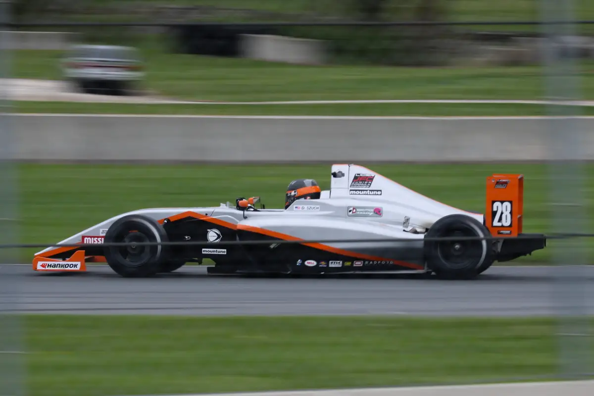 A silver and orange formula race car with the number 28 is speeding along a racetrack.