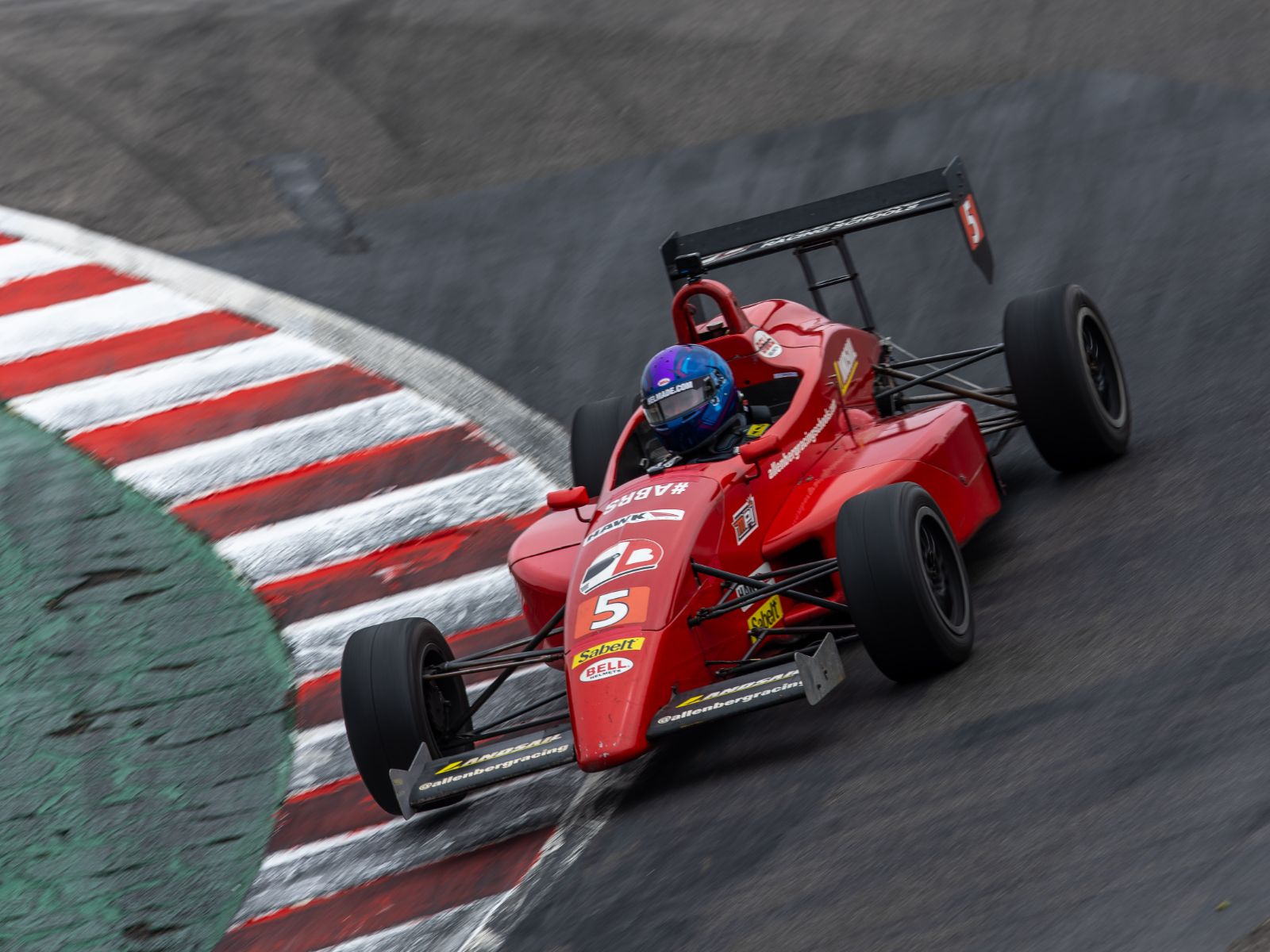 Red open-wheel formula race car taking a corner at speed on a professional road course