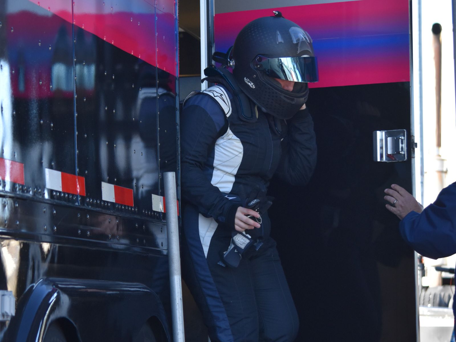 Formula race driver in full racing suit and helmet stepping out of a team trailer at the track