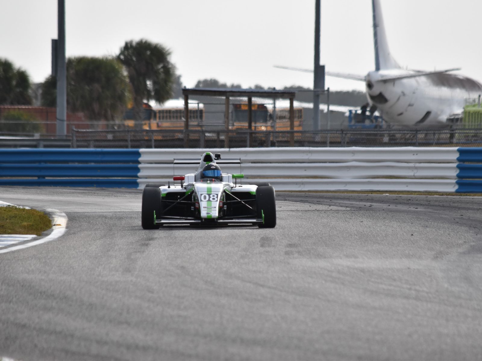Front view of open-wheel formula race car number 08 driving on a racetrack with barriers in background