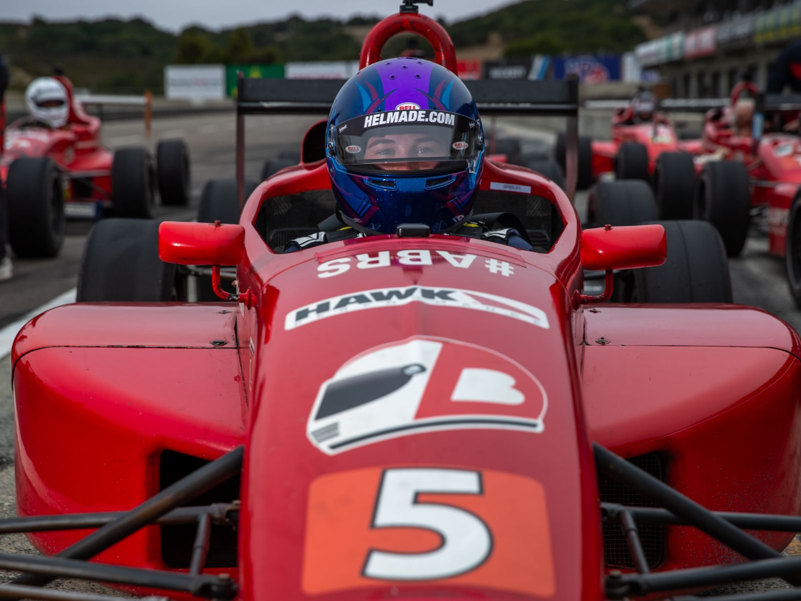Close-up of driver seated in red open-wheel formula race car on the starting grid
