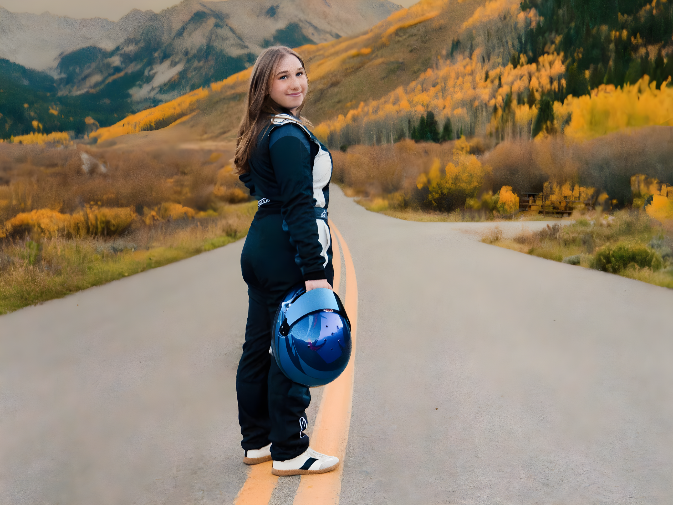 Young racing driver in a full racing suit holding a helmet while standing on a scenic mountain road in autumn